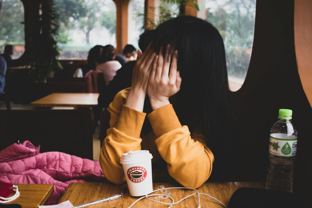 A person covers their face with their hands in a coffee shop.