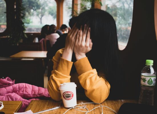 A person covers their face with their hands in a coffee shop.