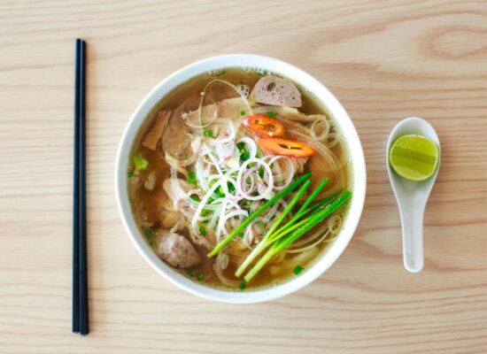 Bowl of Vietnamese pho with chopsticks, spoon, and lime wedge.