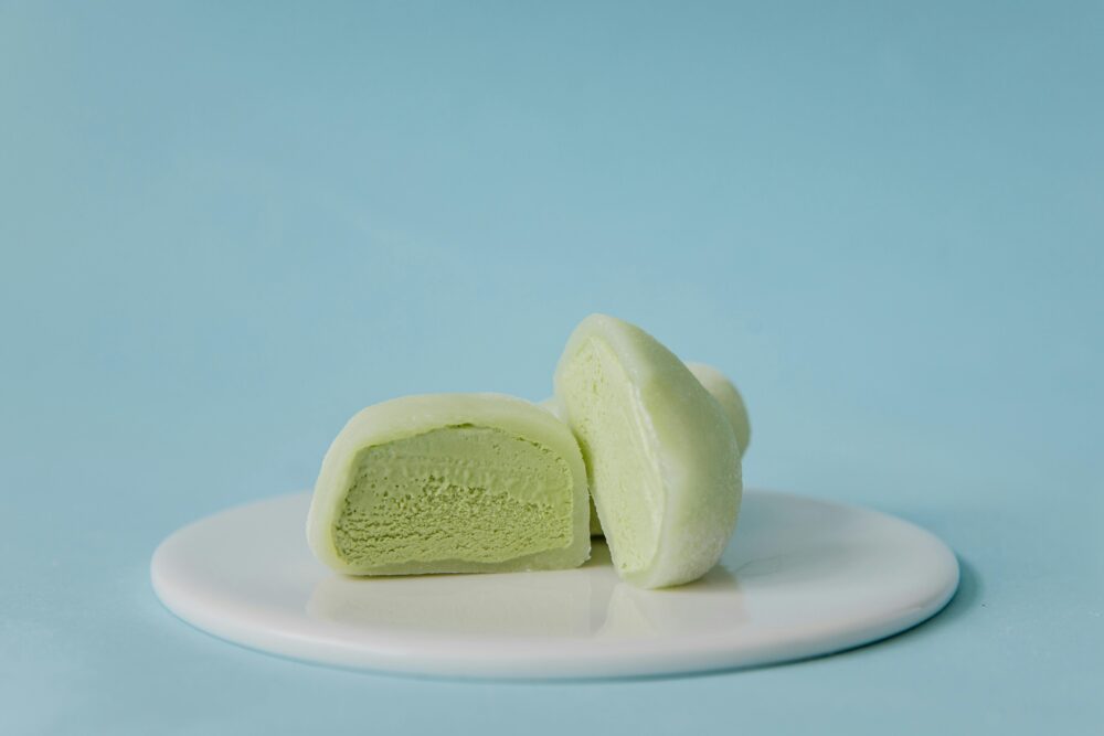 Green mochi ice cream halves on a white plate, blue background.