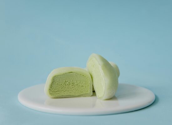 Green mochi ice cream halves on a white plate, blue background.