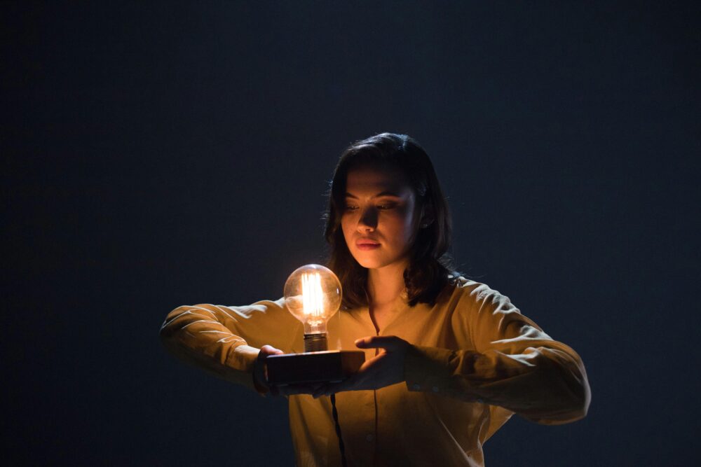 A person holds a glowing lightbulb on a dark background.