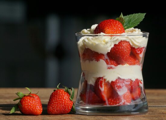 Glass filled with strawberries and cream, garnished with mint leaf.