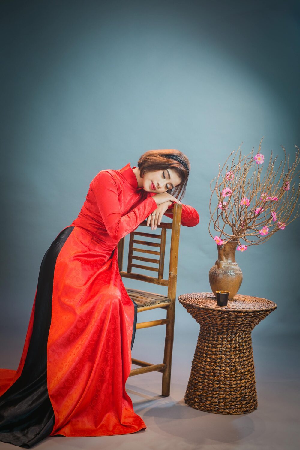 Person in red dress resting on chair beside flower vase.