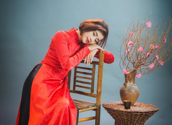 Person in red dress resting on chair beside flower vase.