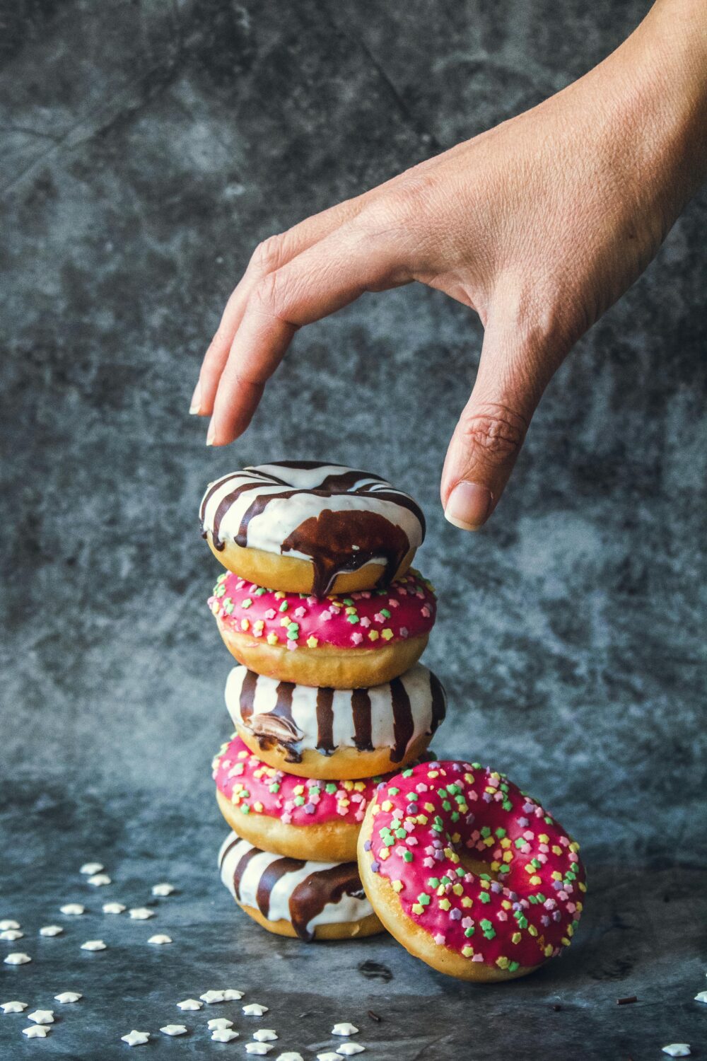 Hand reaching for stacked donuts with colorful icing and sprinkles.