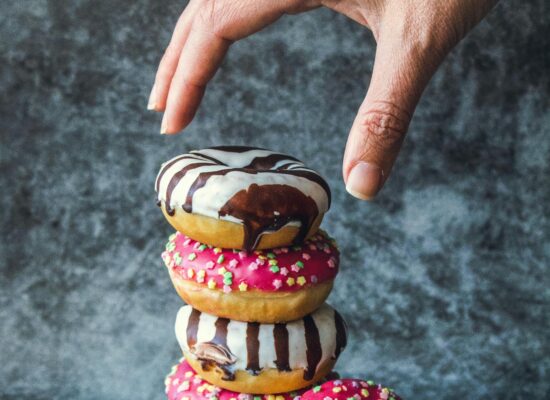 Hand reaching for stacked donuts with colorful icing and sprinkles.