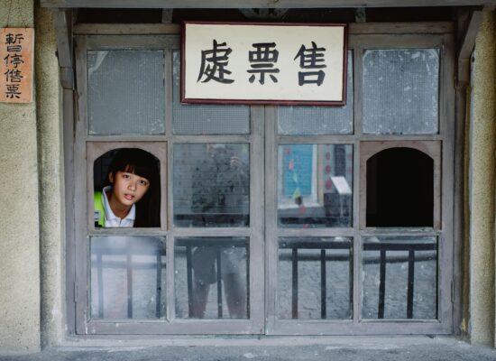 A person looks out of a window with Chinese signs.