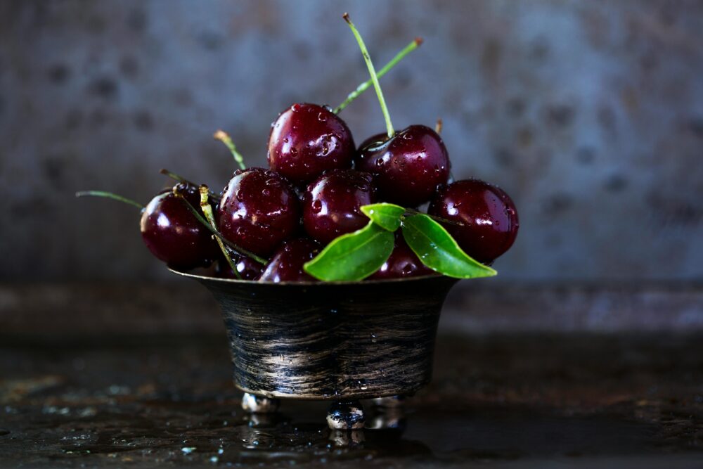 A bowl of fresh cherries with green leaves, water droplets.