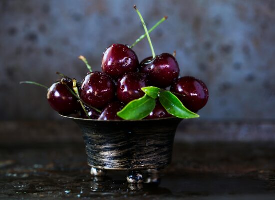 A bowl of fresh cherries with green leaves, water droplets.