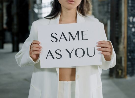 Person in white suit holding sign saying 'SAME AS YOU'.