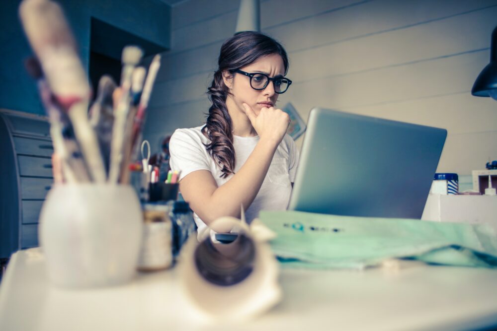 Person sitting at desk, looking thoughtfully at laptop screen.