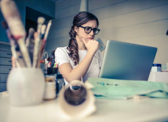 Person sitting at desk, looking thoughtfully at laptop screen.