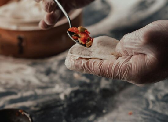 Gloved hands preparing dumplings with filling on a floured surface.