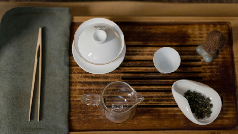 Tea ceremony set with gaiwan, cups, and tea leaves on wooden tray.