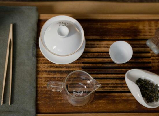 Tea ceremony set with gaiwan, cups, and tea leaves on wooden tray.