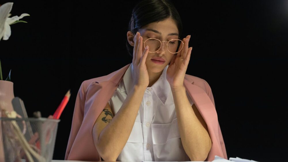 Person with glasses rubbing temples at a desk with papers.