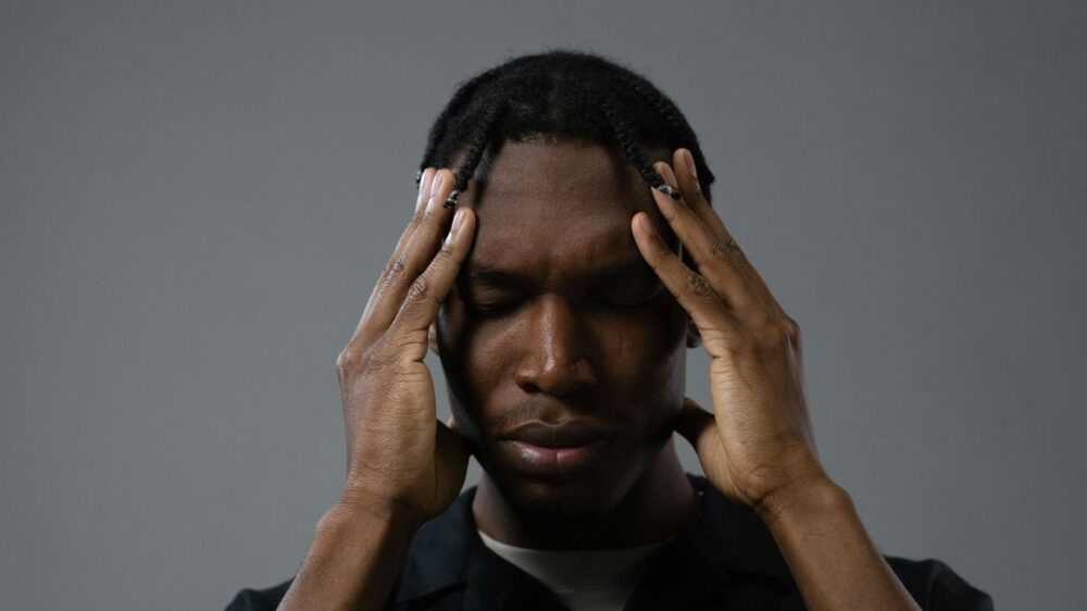 Person with hands on temples, eyes closed, appearing stressed or thoughtful.