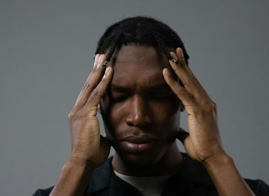 Person with hands on temples, eyes closed, appearing stressed or thoughtful.