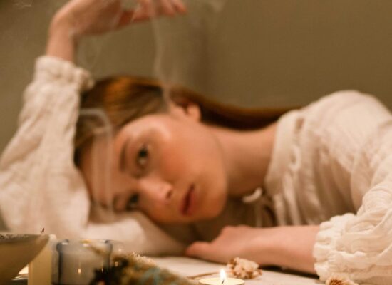 Person resting head on table with candles and dried flowers.
