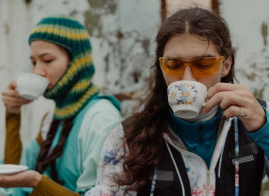 Two people outdoors, drinking tea, wearing colorful winter clothing.
