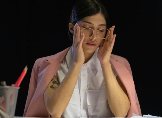 Person with glasses rubbing temples at a desk with papers.