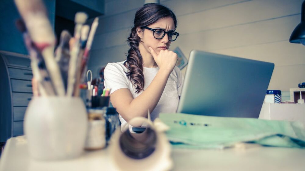 Person sitting at desk, looking thoughtfully at laptop screen.