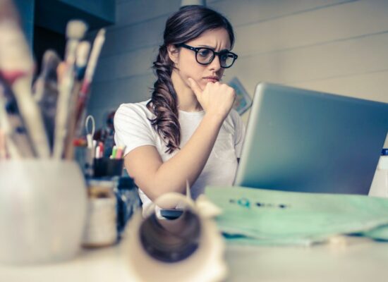 Person sitting at desk, looking thoughtfully at laptop screen.