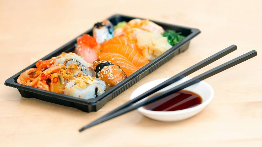 Assorted sushi in a tray with chopsticks and soy sauce.