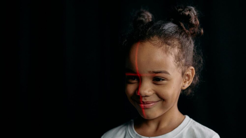 Smiling child with red lines on face, dark background.