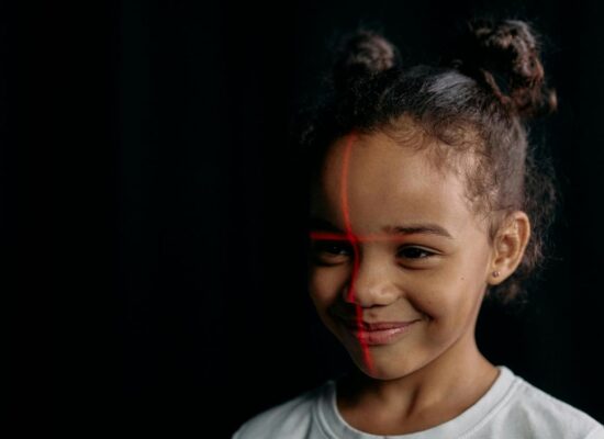 Smiling child with red lines on face, dark background.