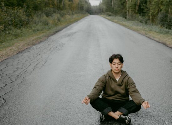 Person meditating on empty road surrounded by green forest.