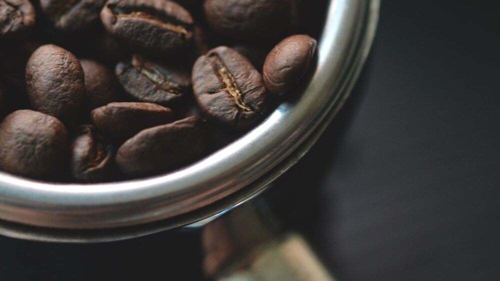 Close-up of coffee beans in a metal portafilter, dark background.