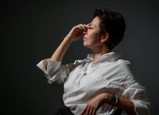 Person in white shirt sitting, pinching nose, looking stressed.