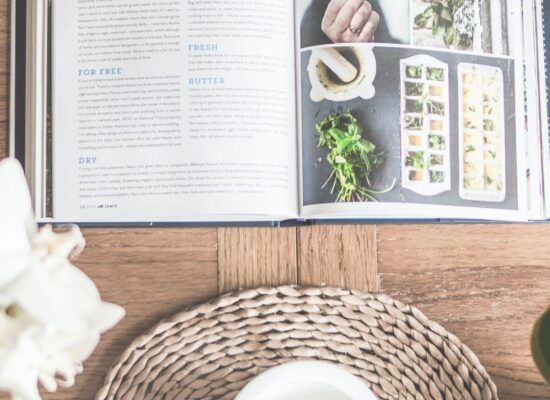 Open cookbook about herbs, mortar and pestle, wooden table.