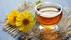 Glass cup of tea with yellow flowers on burlap mat.