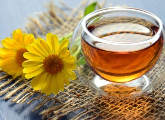 Glass cup of tea with yellow flowers on burlap mat.