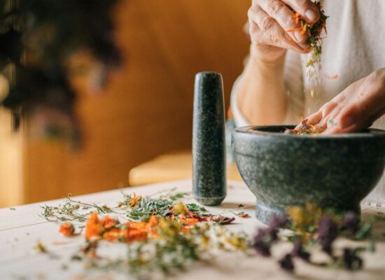 Person preparing dried herbs with mortar and pestle on table.