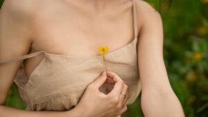 Person in beige dress holding small yellow flower to chest.