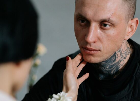 Person with tattoos being gently touched on the face, emotional moment.