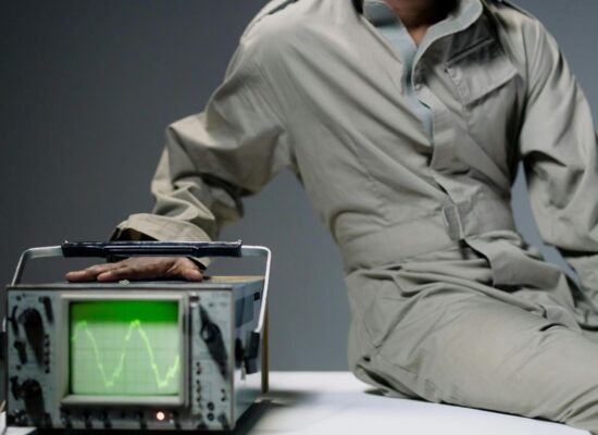 Person in jumpsuit with hand on oscilloscope displaying waveform.