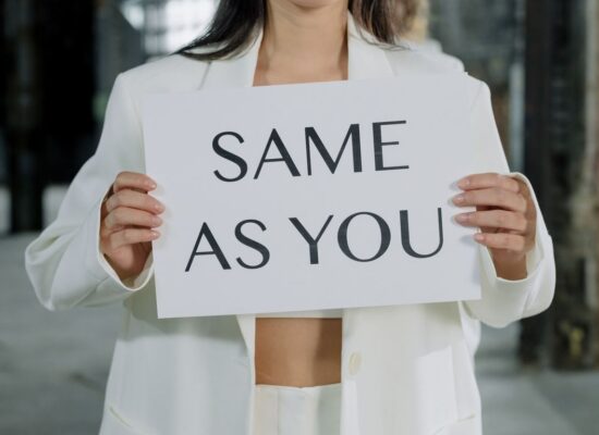 Person in white suit holding sign saying 'SAME AS YOU'.