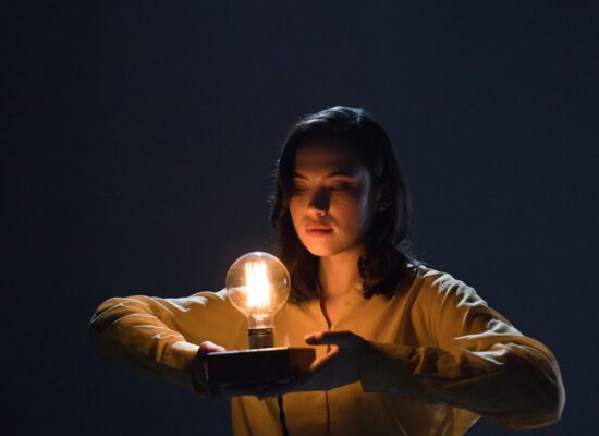 A person holds a glowing lightbulb on a dark background.