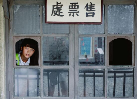 A person looks out of a window with Chinese signs.