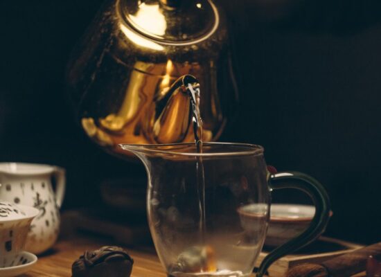 Golden teapot pouring water into a glass pitcher during tea ceremony.
