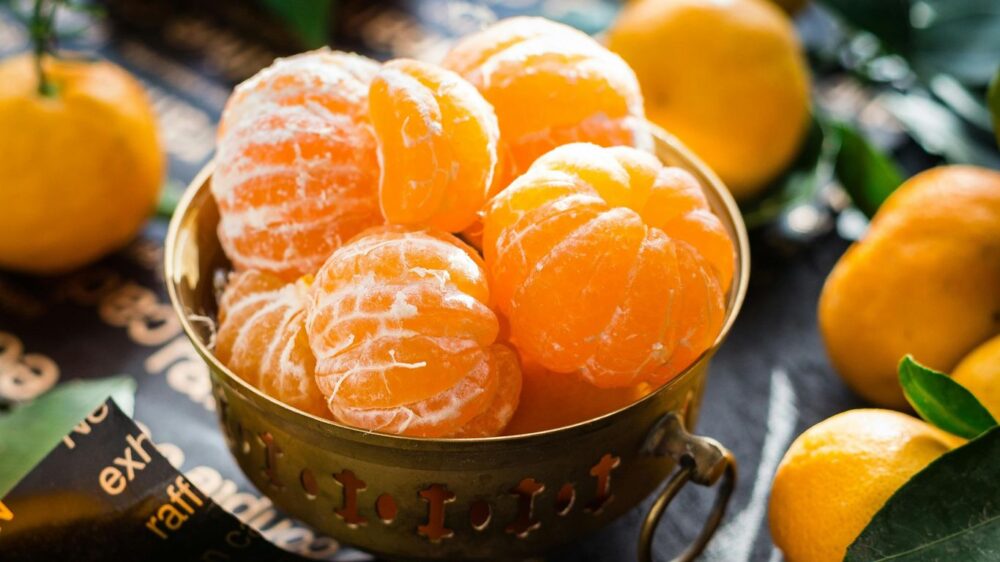 Peeled tangerines in a brass bowl surrounded by whole tangerines.