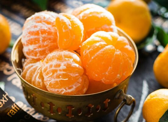 Peeled tangerines in a brass bowl surrounded by whole tangerines.