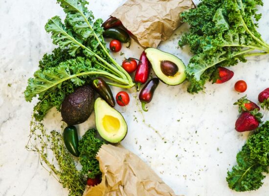 Fresh vegetables and fruits, including kale, avocado, strawberries, tomatoes.