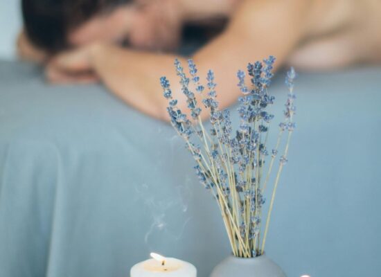 Person receiving massage, candles and lavender create relaxing atmosphere.