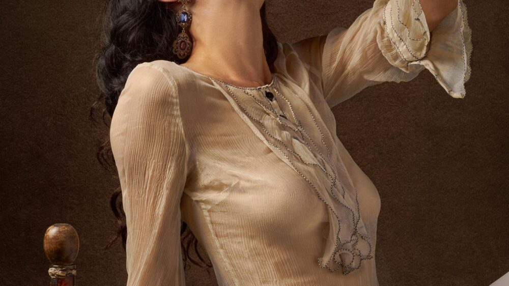 Person holding grapes, surrounded by fruit and elegant objects.